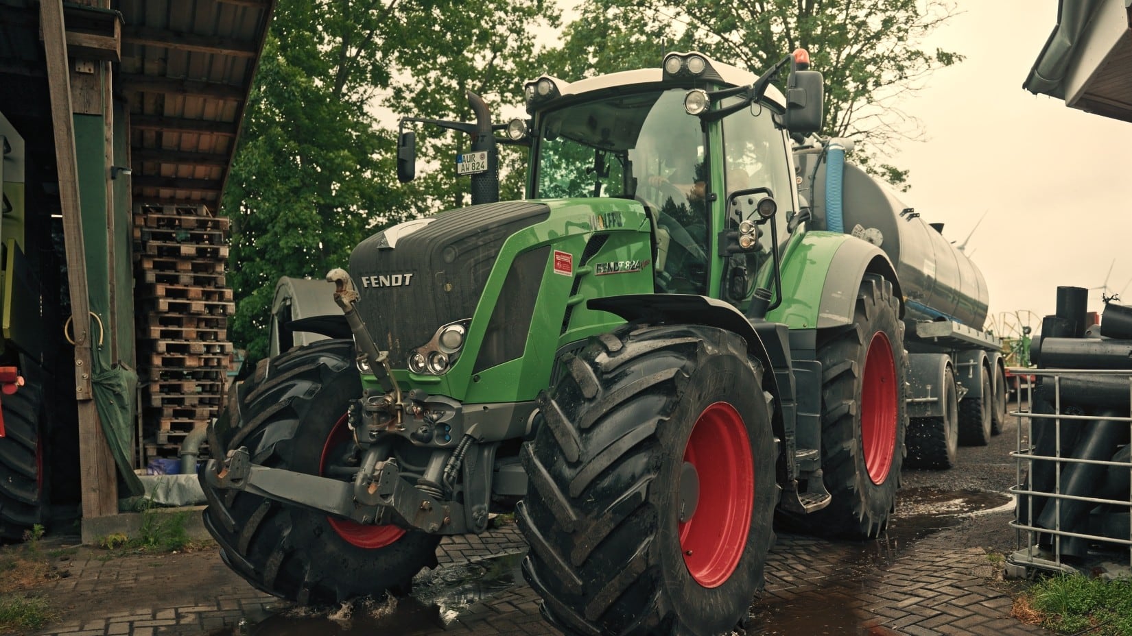 Fendt mit Güllefass fährt durch eine Pfütze auf dem Hof