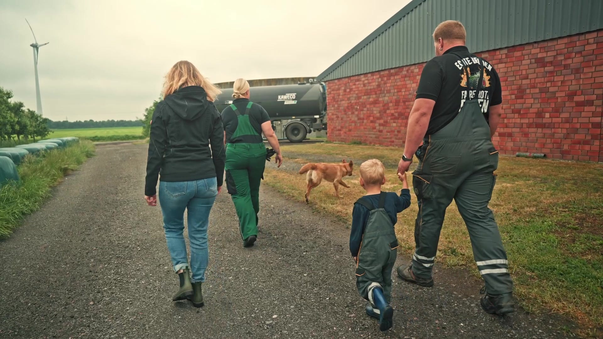 Zwei Frauen, ein Landwirt mit seinem Sohn und ein Hund gehen gemeinsam den Hofweg entlang