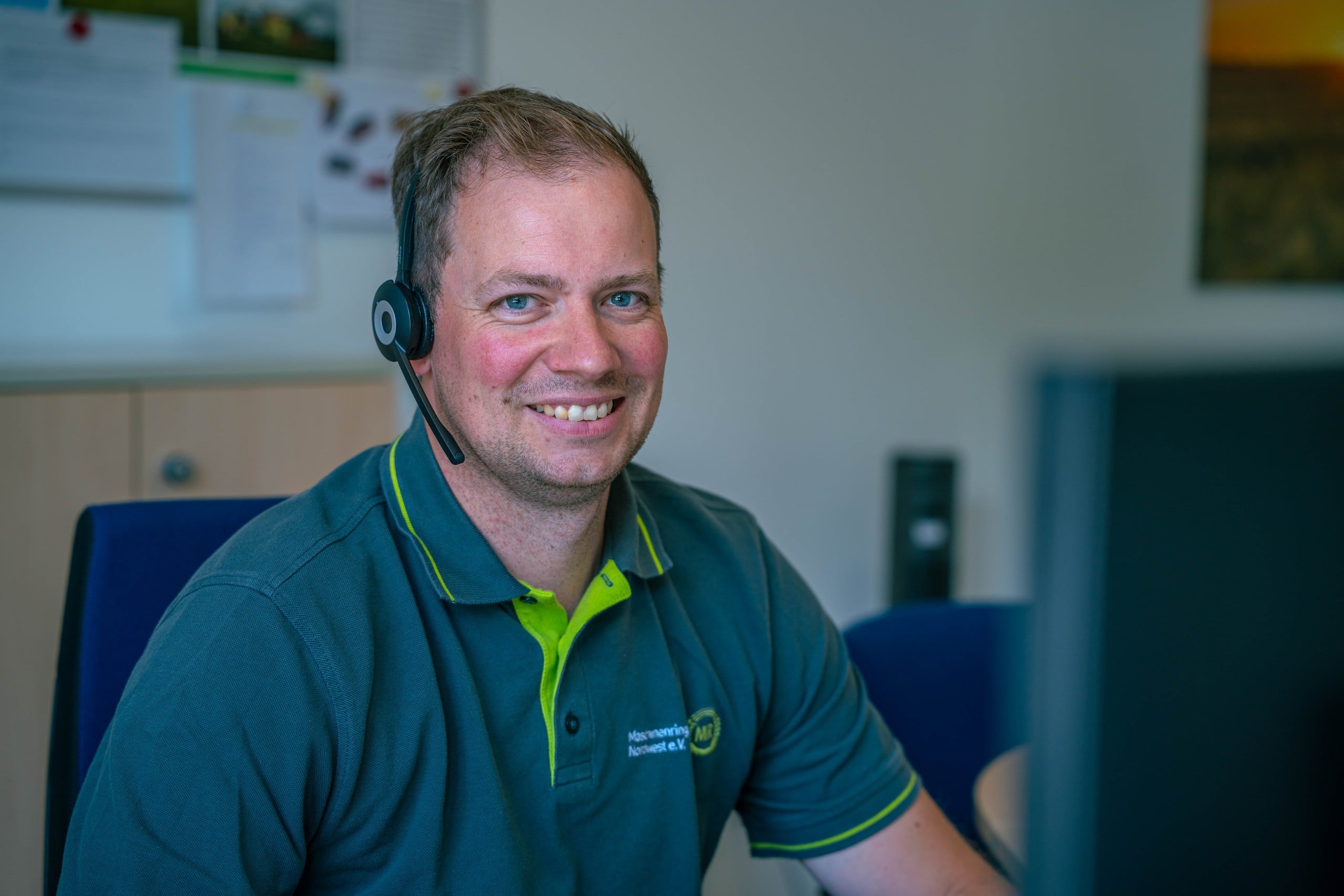 Kollege aus der Geschäftsstelle mit Headset lacht in die Kamera